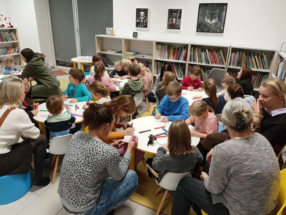 Dzieci i rodzice rysują przy stolikach.